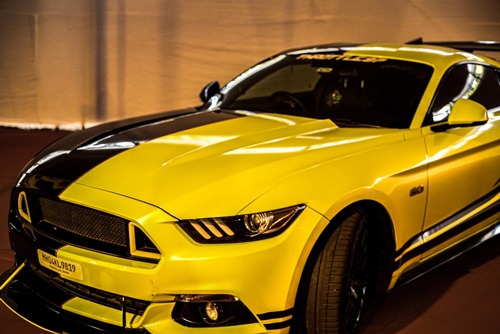 a yellow mustang car with black stripes parked in a garage