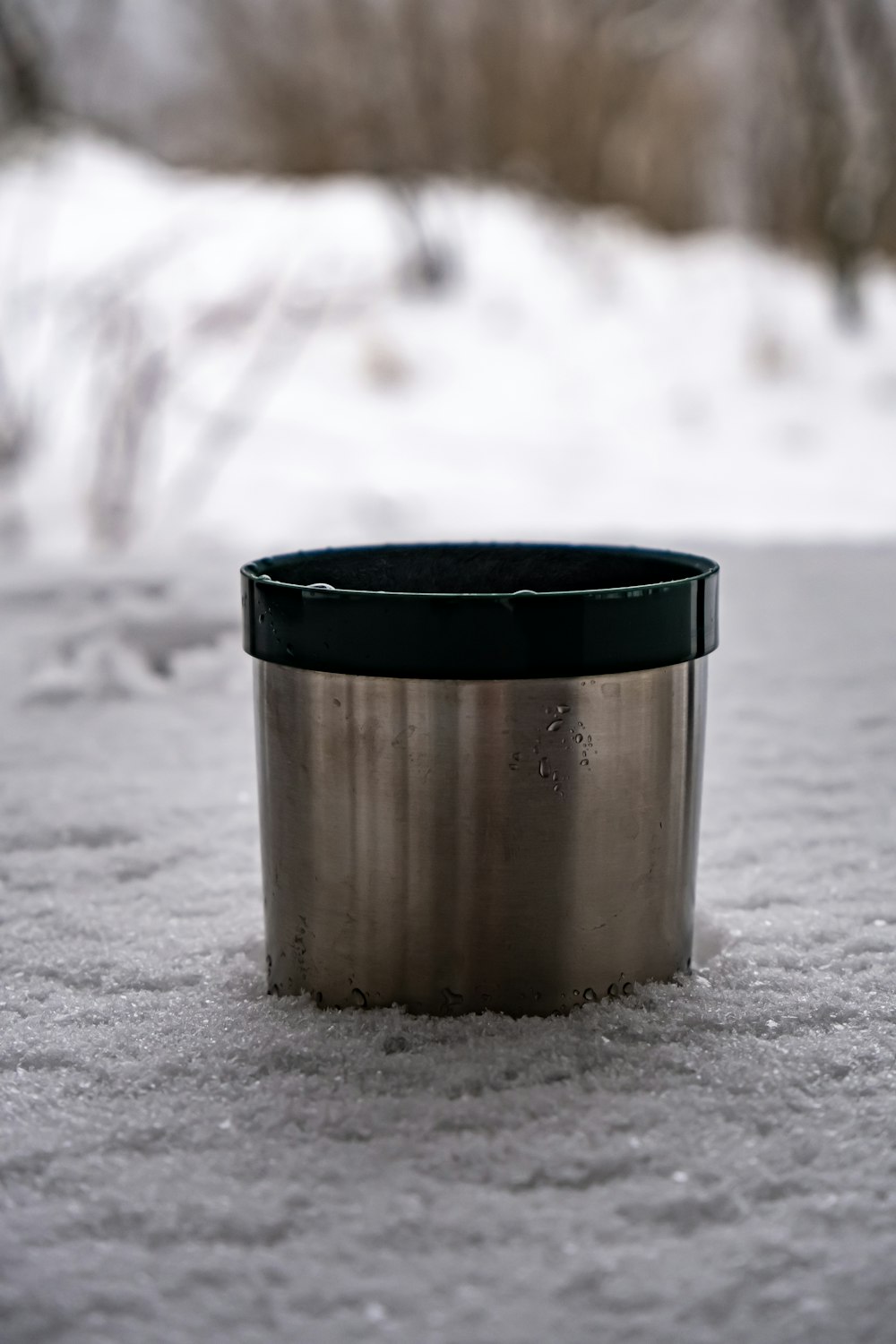 a metal cup sitting on top of snow covered ground