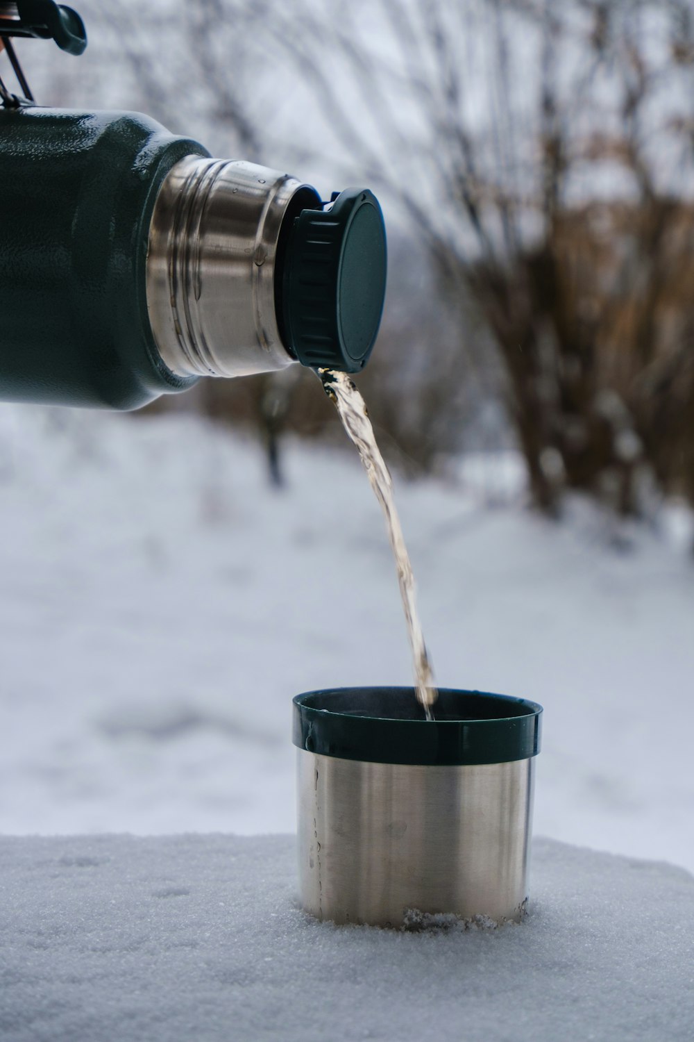 una persona vertiendo agua en una taza en la nieve