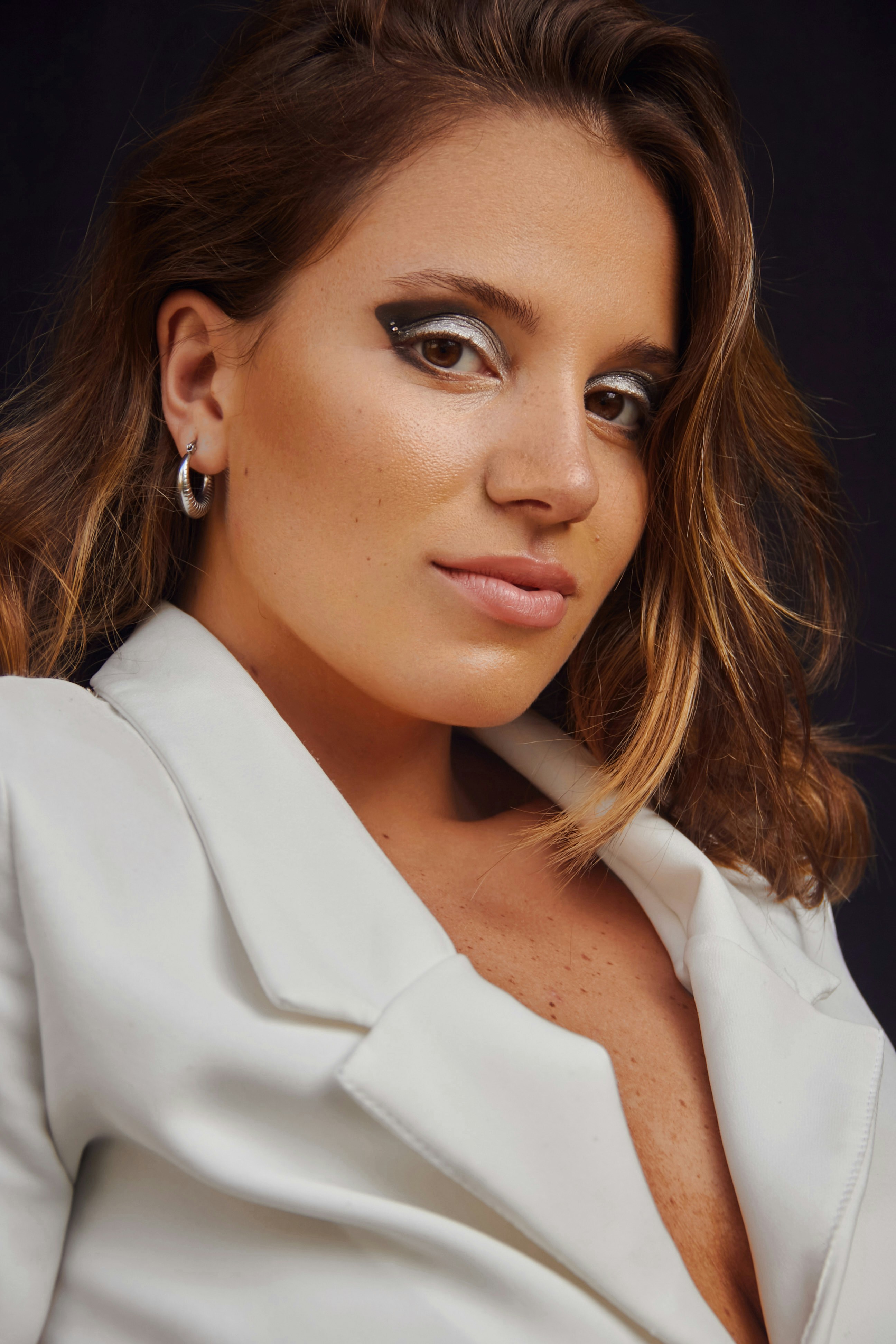 a woman wearing a white jacket and earrings