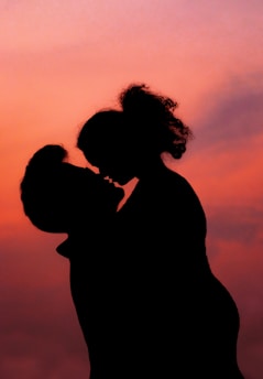 A tasteful, artistic silhouette of a couple embracing against a warm pink background.