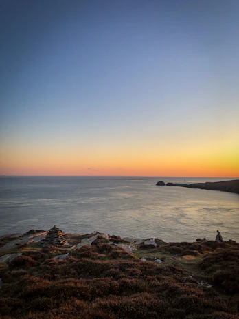 A serene Mediterranean coastline at sunset with soft stone textures in the foreground.