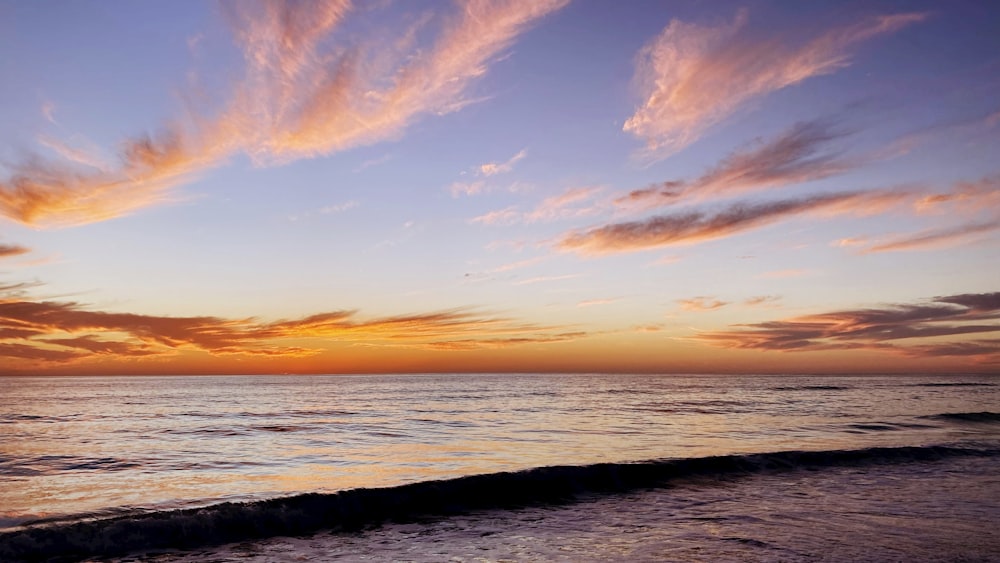 a sunset over the ocean with clouds in the sky