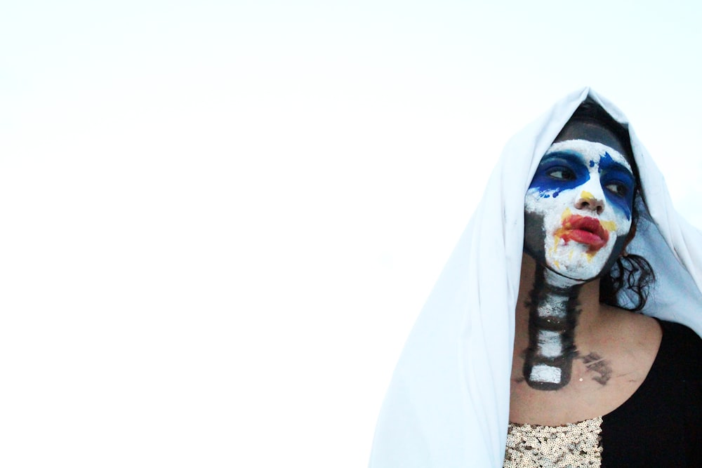 a woman with a painted face hiding behind a blanket