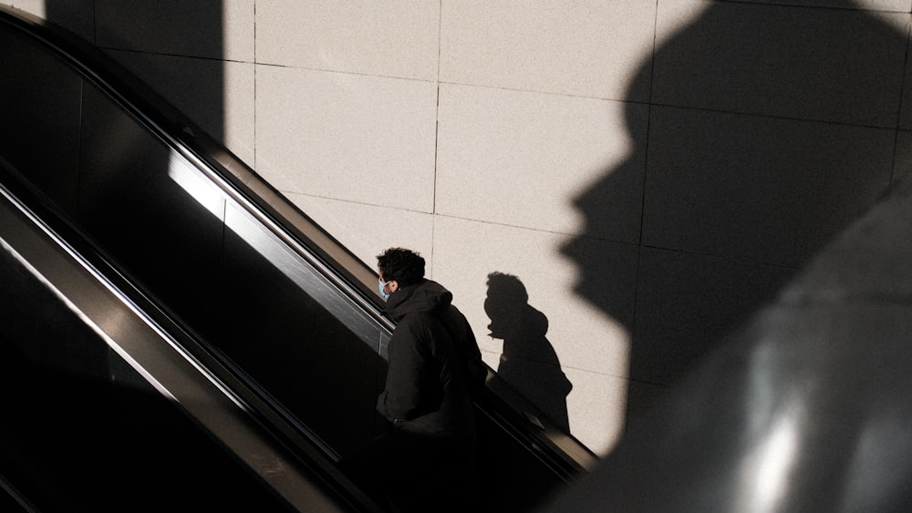a man riding an escalator next to a shadow of a person