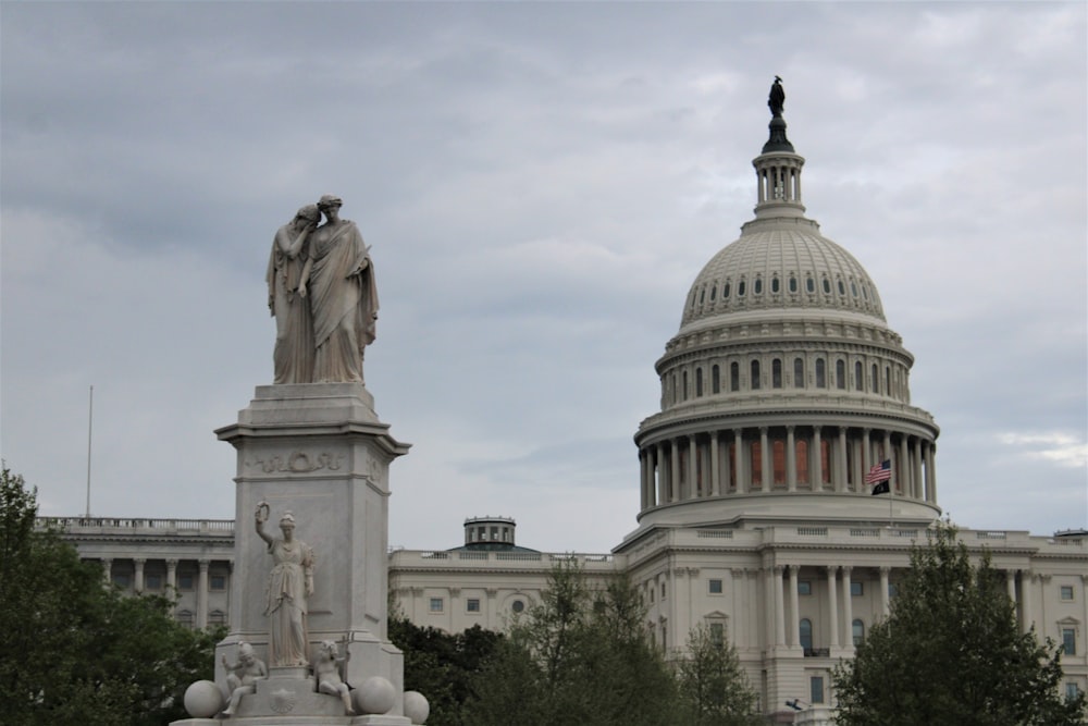 a statue stands in front of the capitol building
