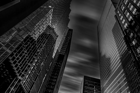 A dramatic black and white shot of city skyscrapers piercing through low-hanging clouds