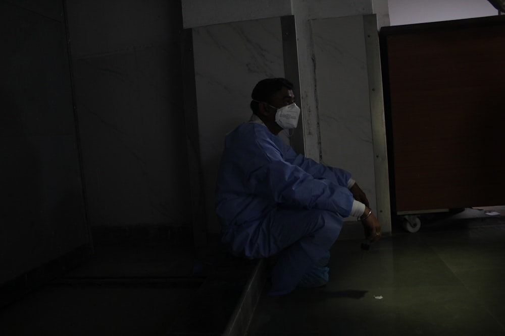 a man in a blue coat and mask sitting on a bench