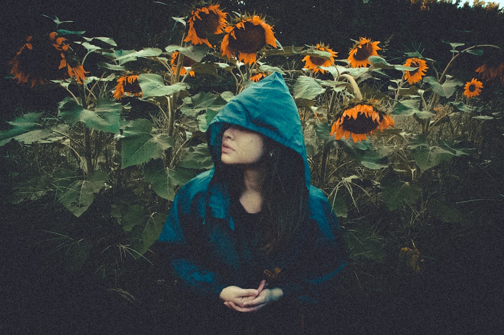 a woman in a blue hoodie sitting in a field of sunflowers