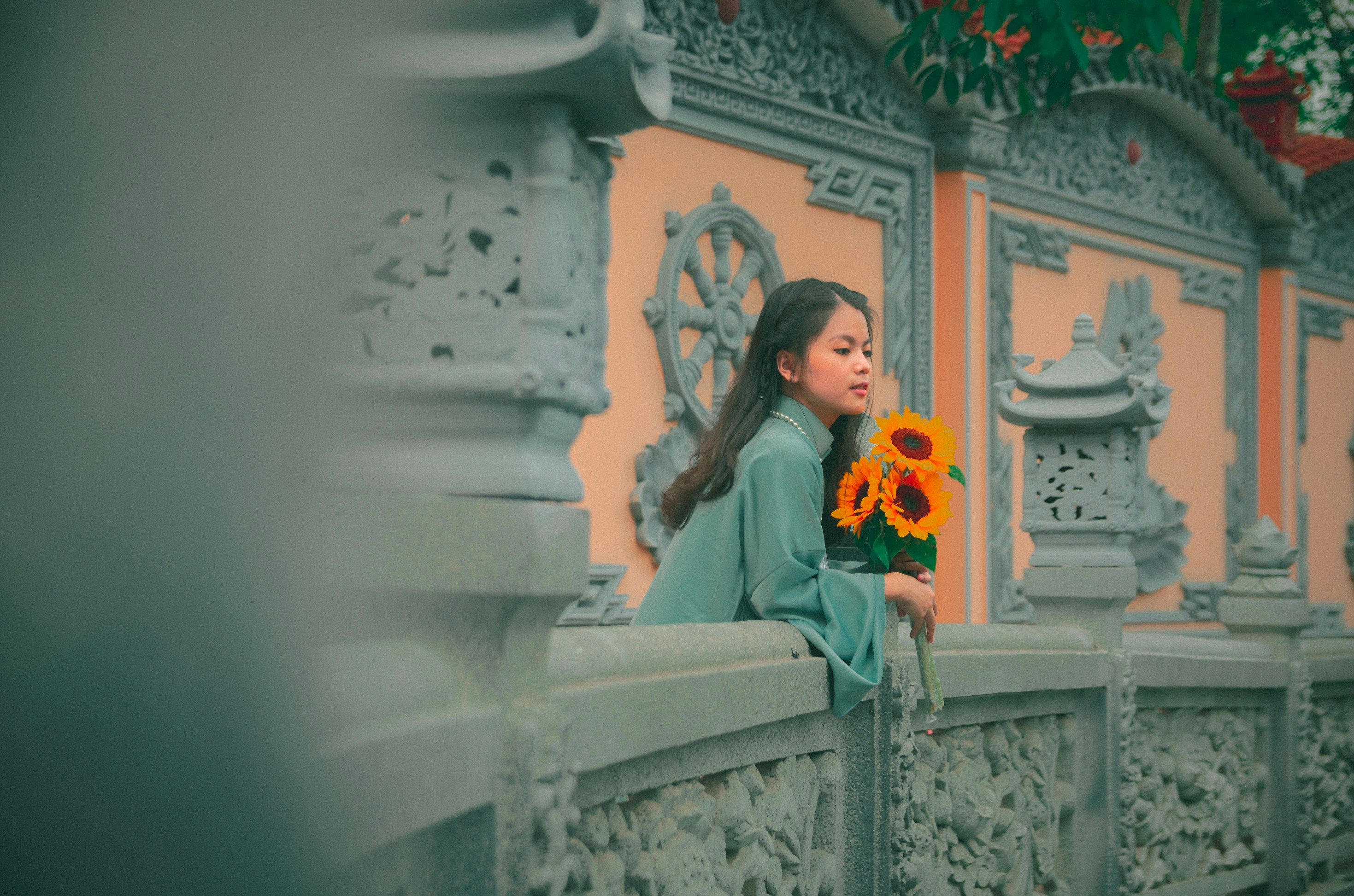 a woman standing on a bridge holding a bunch of sunflowers