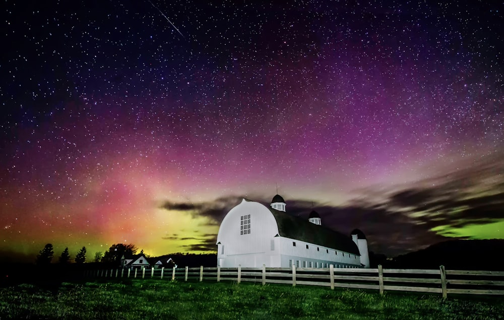a white barn with a purple and green aurora behind it