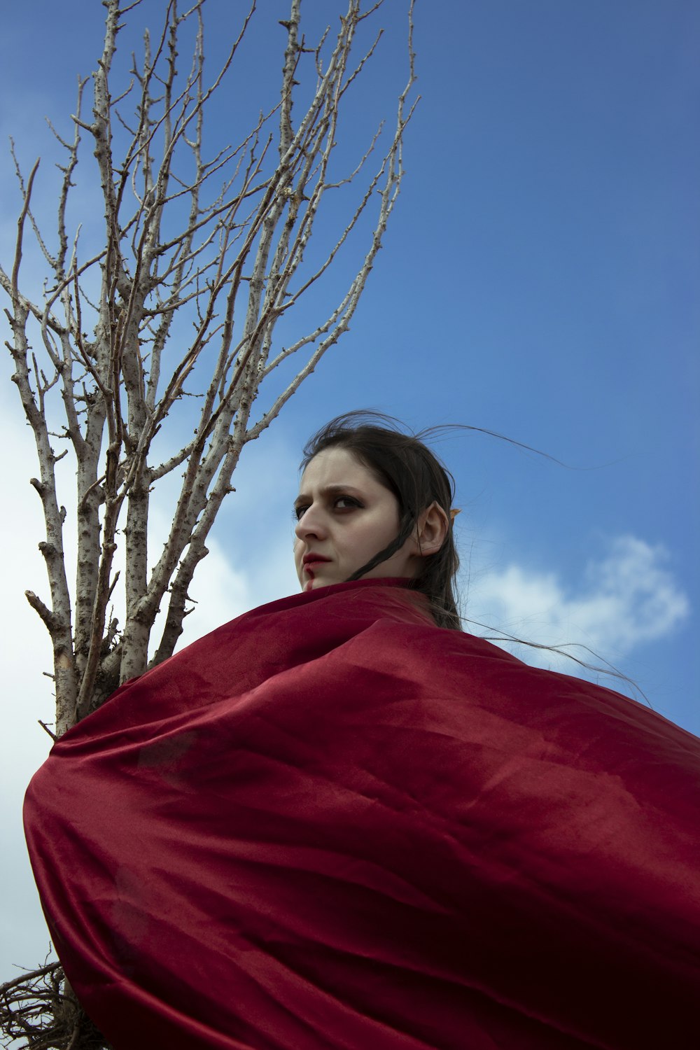 a woman wrapped in a red blanket standing next to a tree