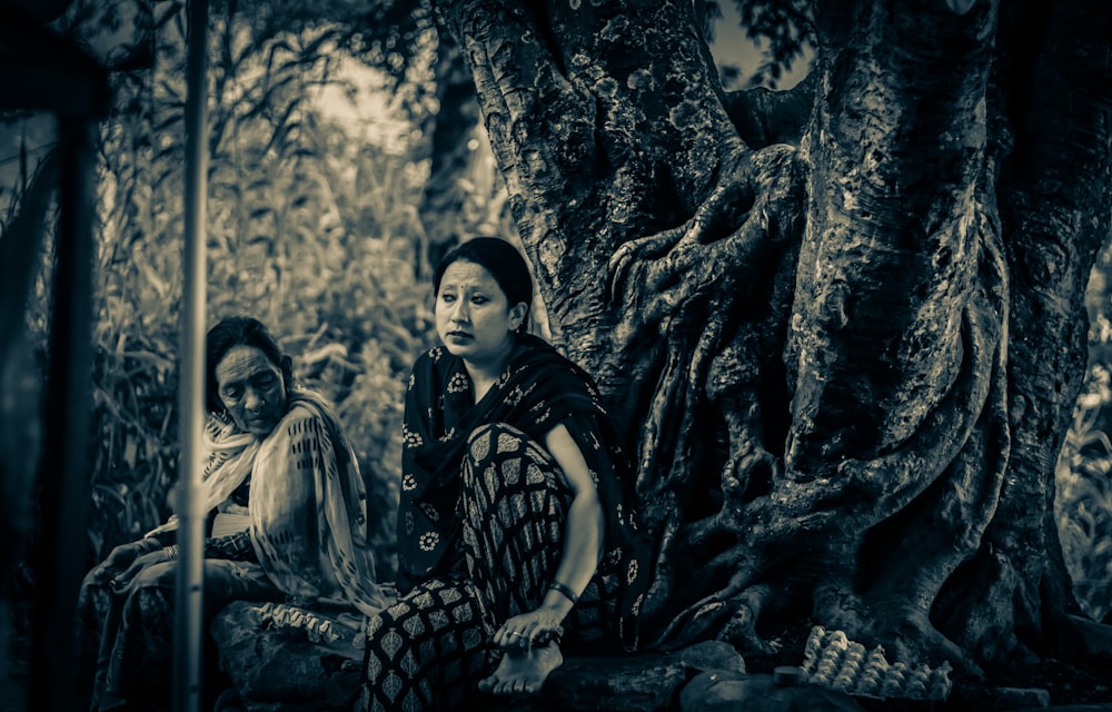 two women sitting next to each other under a tree