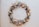 A circular wreath made of dried flowers and foliage, featuring a mix of creamy whites, soft oranges, and subtle greens. The arrangement includes petals, leaves, and delicate sprigs, creating a rustic and organic aesthetic against a neutral background.