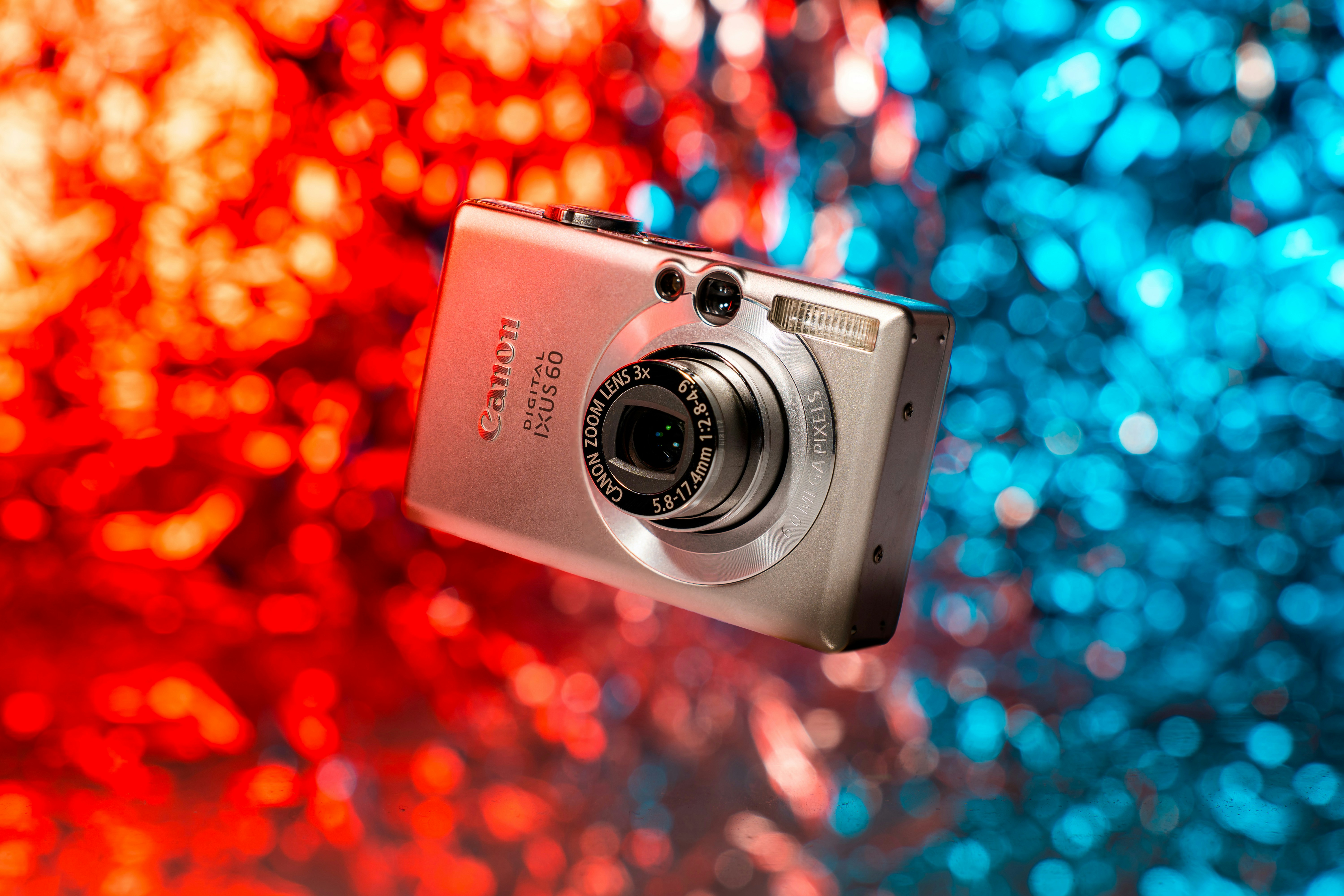 A digital camera is shown in front of a colorful background photo