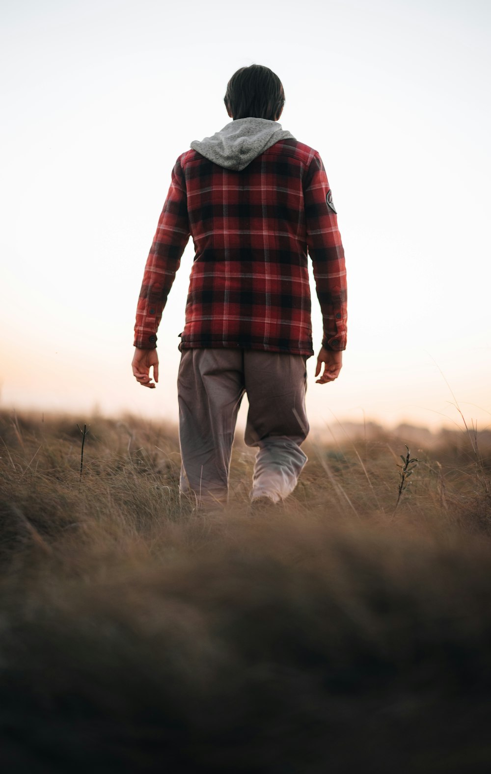 a man walking through a field at sunset