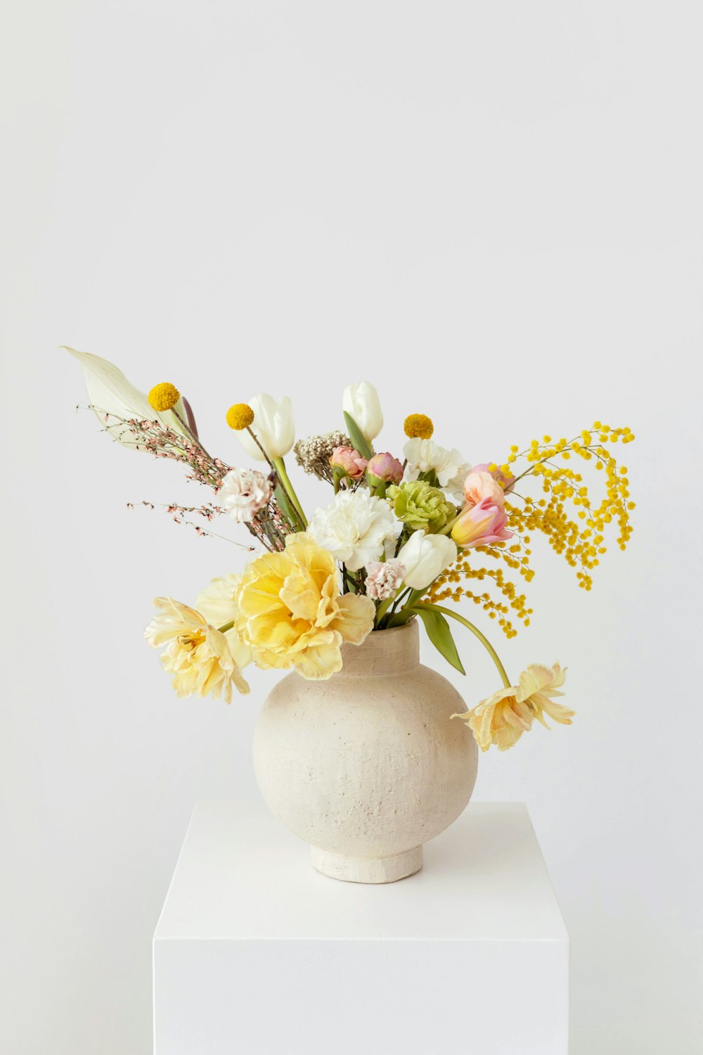 um vaso branco com flores amarelas e brancas nele