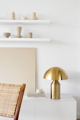 a white room with a gold lamp and a wicker chair