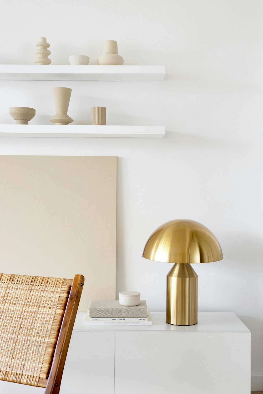 a white room with a gold lamp and a wicker chair