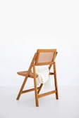 A wooden chair with a woven backrest is positioned against a plain white background. A white knit blanket is draped over the seat, adding a soft contrast to the natural wood tones.