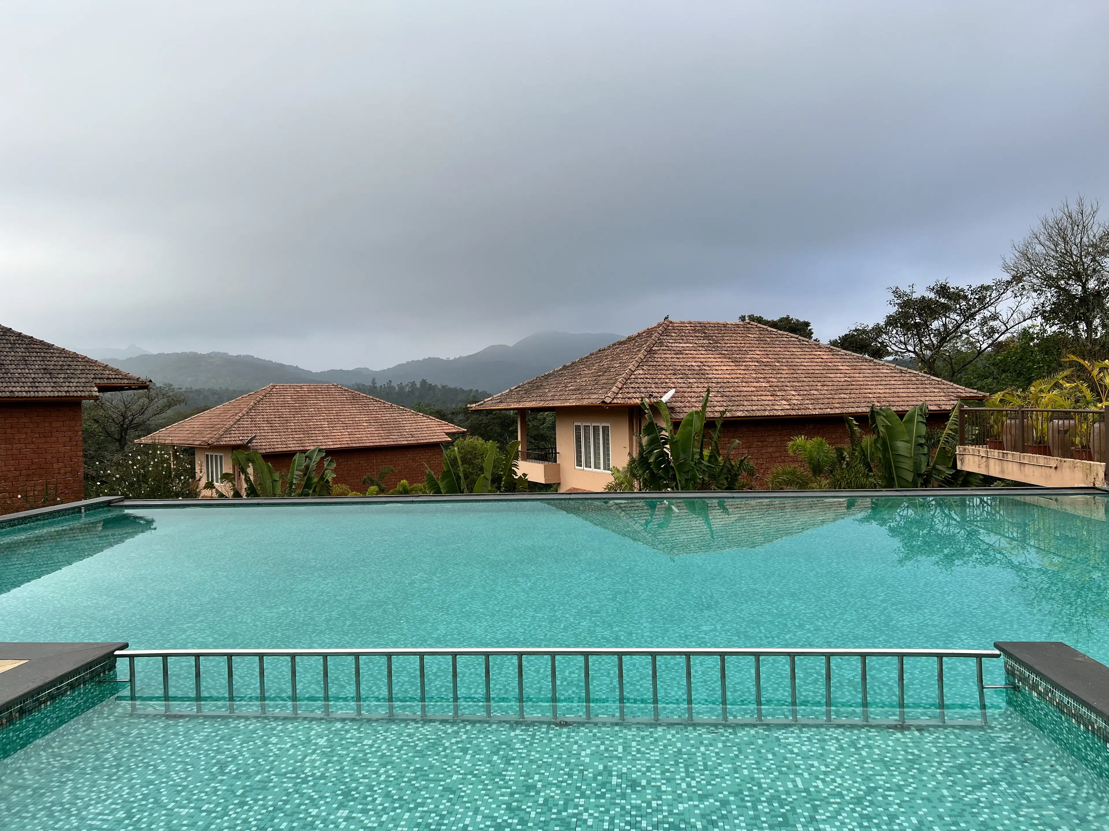 Tiled-roof villas beside a turquoise pool with misty hills beyond