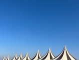 A series of pointed tent tops with alternating black and white stripes stand against a clear blue sky. The tents are arranged in a row, creating a rhythmic pattern across the bottom of the image.