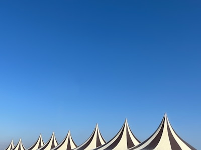 A series of pointed tent tops with alternating black and white stripes stand against a clear blue sky. The tents are arranged in a row, creating a rhythmic pattern across the bottom of the image.