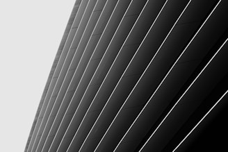 A series of large, angled panels in a monochromatic color scheme create a sleek, modern architectural design. The panels are arranged diagonally and are accentuated by thin, light lines between each one, enhancing the sense of depth and structure.