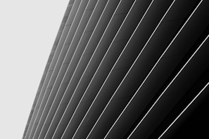 A series of large, angled panels in a monochromatic color scheme create a sleek, modern architectural design. The panels are arranged diagonally and are accentuated by thin, light lines between each one, enhancing the sense of depth and structure.