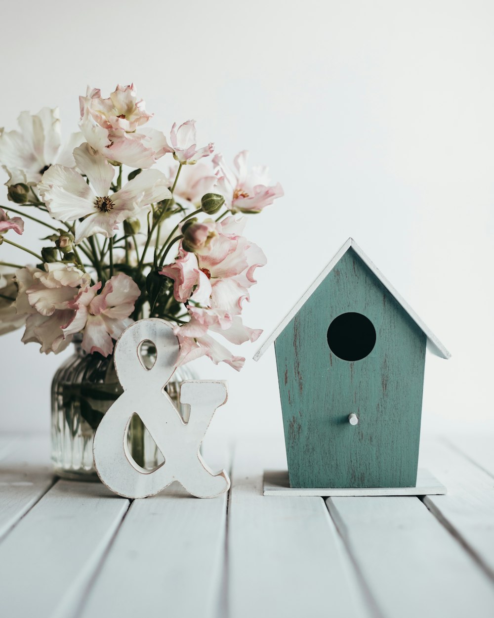 a wooden birdhouse next to a vase of flowers