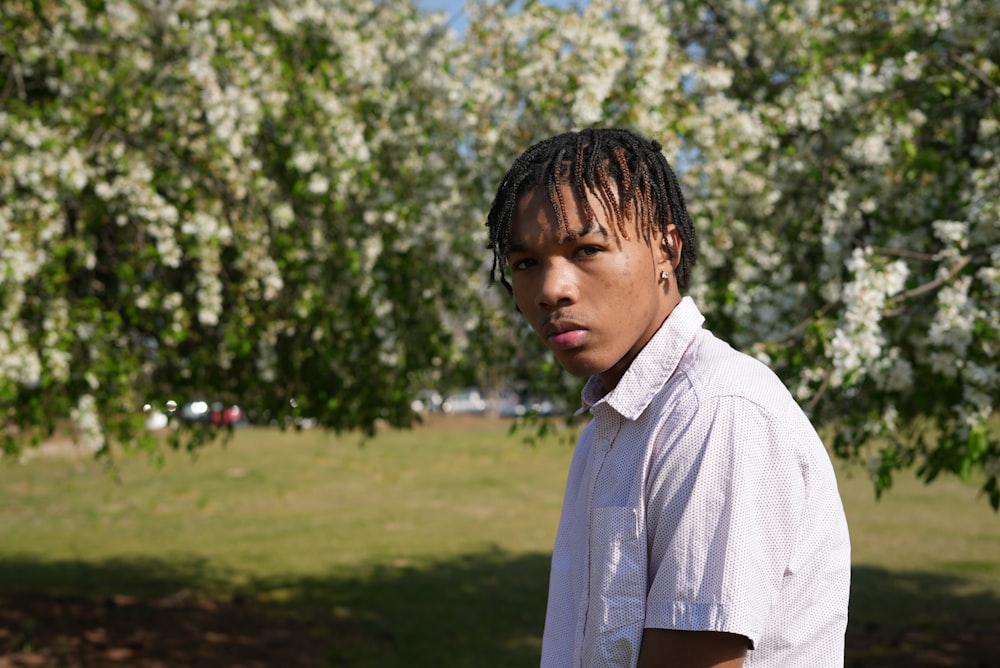 a man with dreadlocks standing in front of a tree