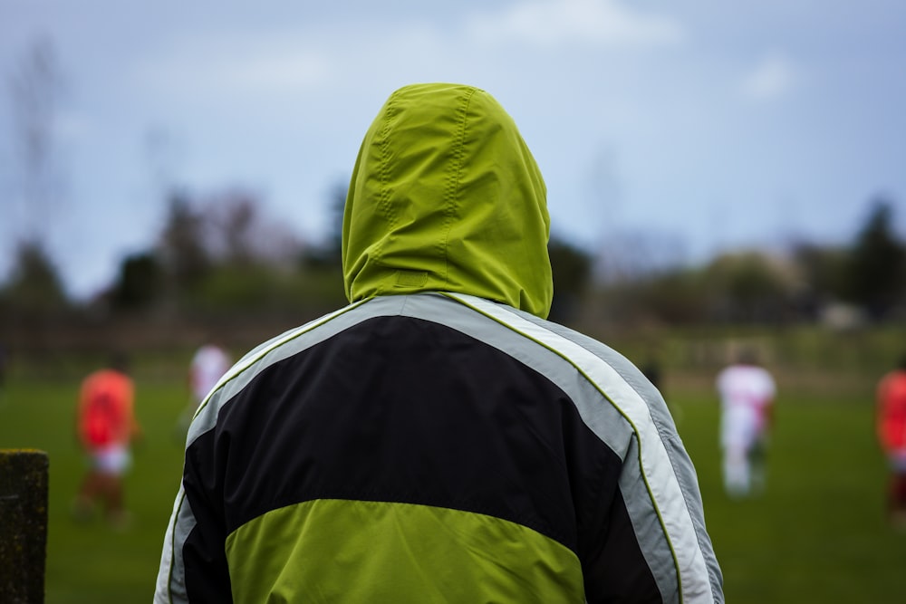 a person in a green and black jacket watching a soccer game