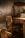 A rustic, dimly lit room featuring a wooden chair and desk. The furniture has a vintage appearance with a slightly distressed finish. A spindle and other woodworking tools are visible, suggesting the room might be a workshop or studio. The walls are bare with subtle cracks, adding to the aged atmosphere.