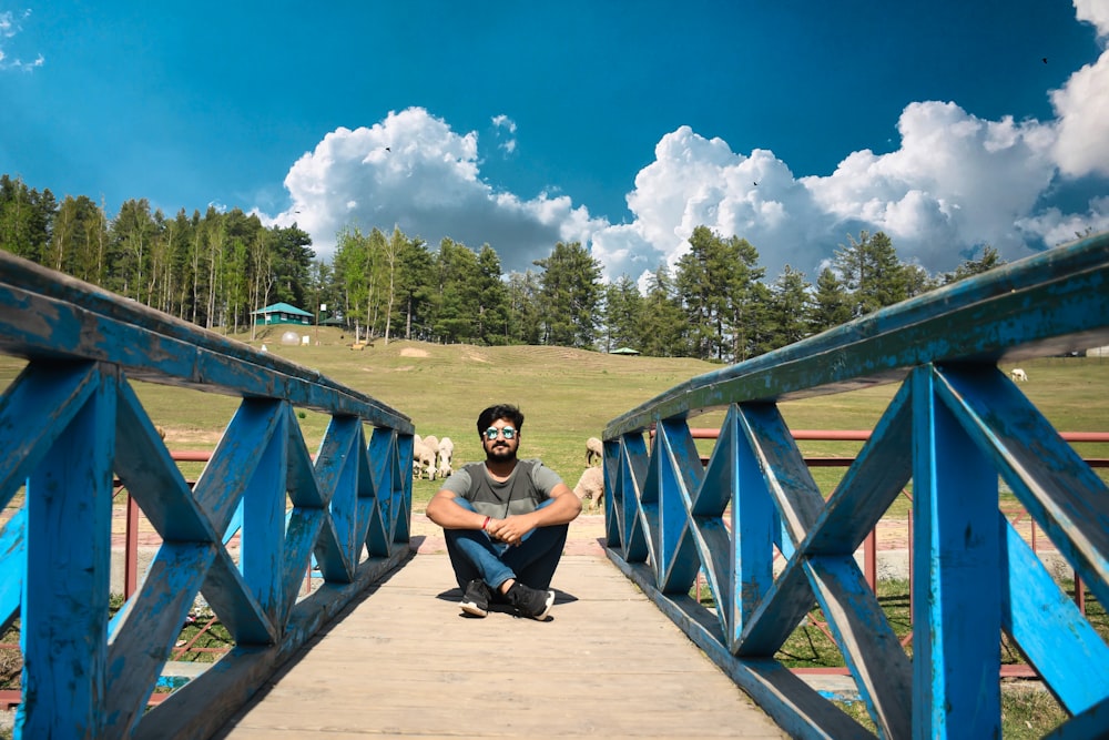 a man sitting on a bridge with a cow in the background