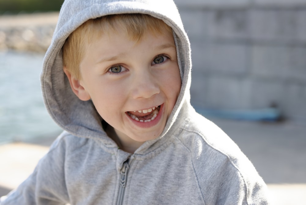 Ein kleiner Junge trägt einen grauen Kapuzenpullover und lächelt