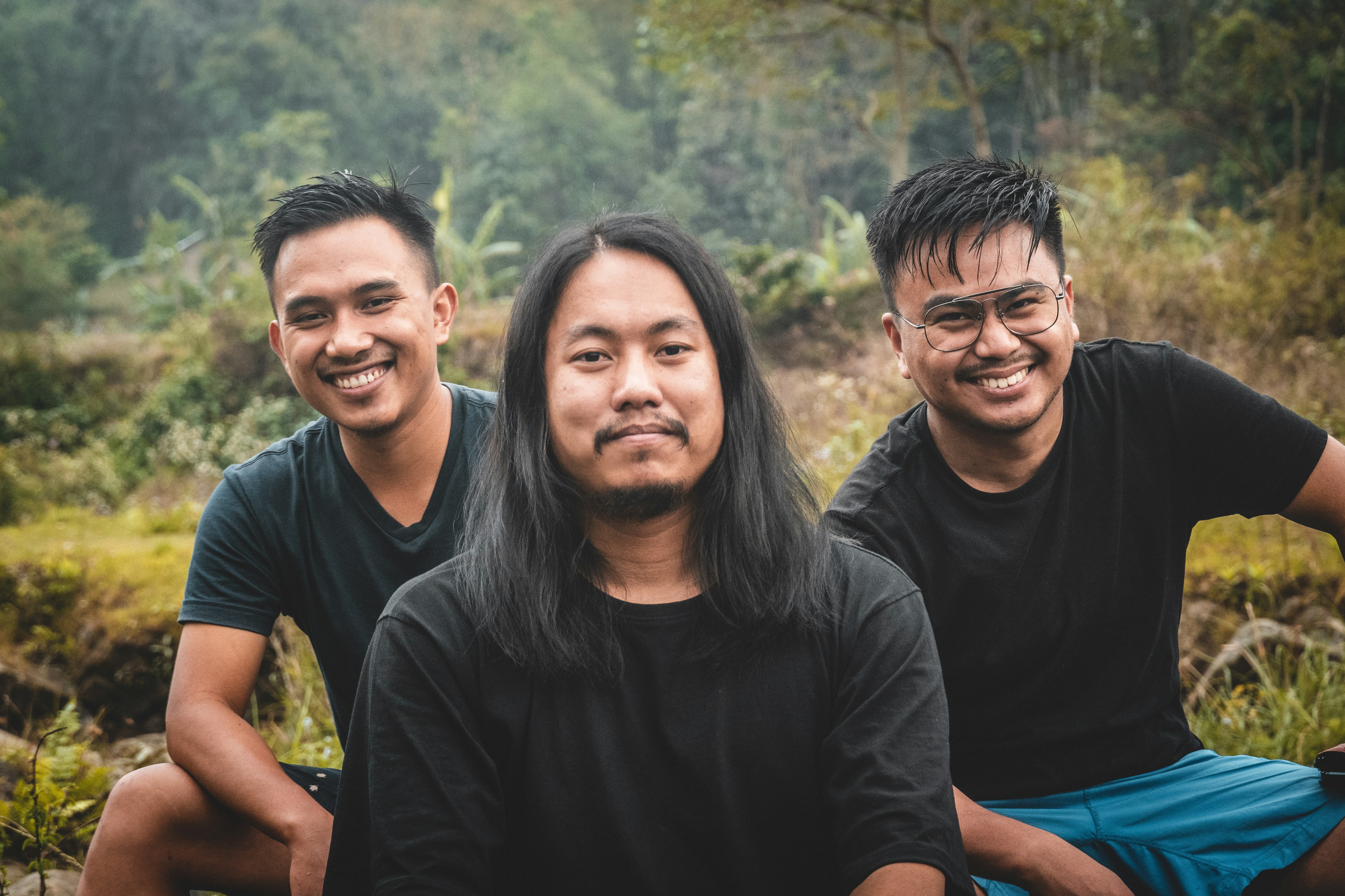 three men sitting next to each other in a forest