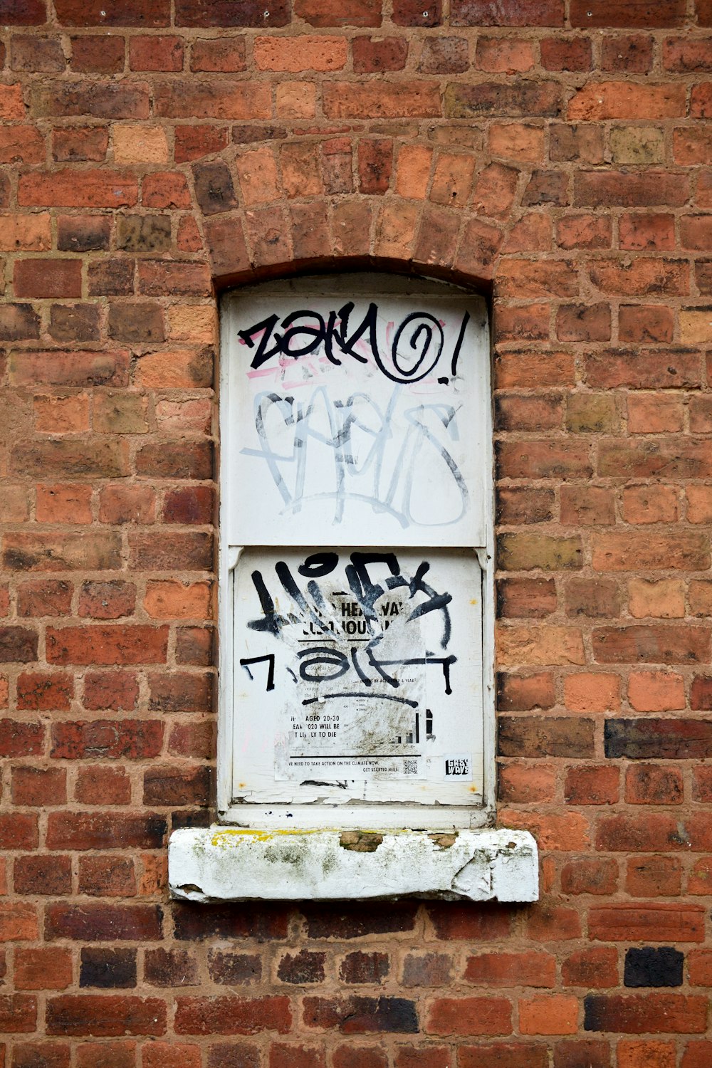 un mur de briques avec une fenêtre avec des graffitis dessus