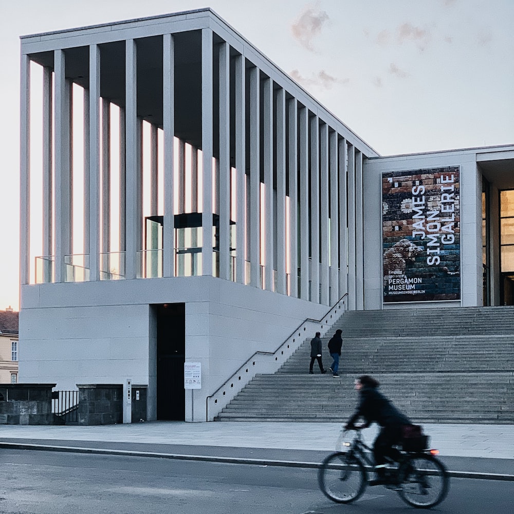 a man riding a bike past a tall building