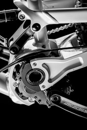 A close-up view of a bicycle's mechanical components, including the frame, chainring, and part of the chain. The image focuses on the intricate details of the bike's engineering, highlighting metallic textures and joints.