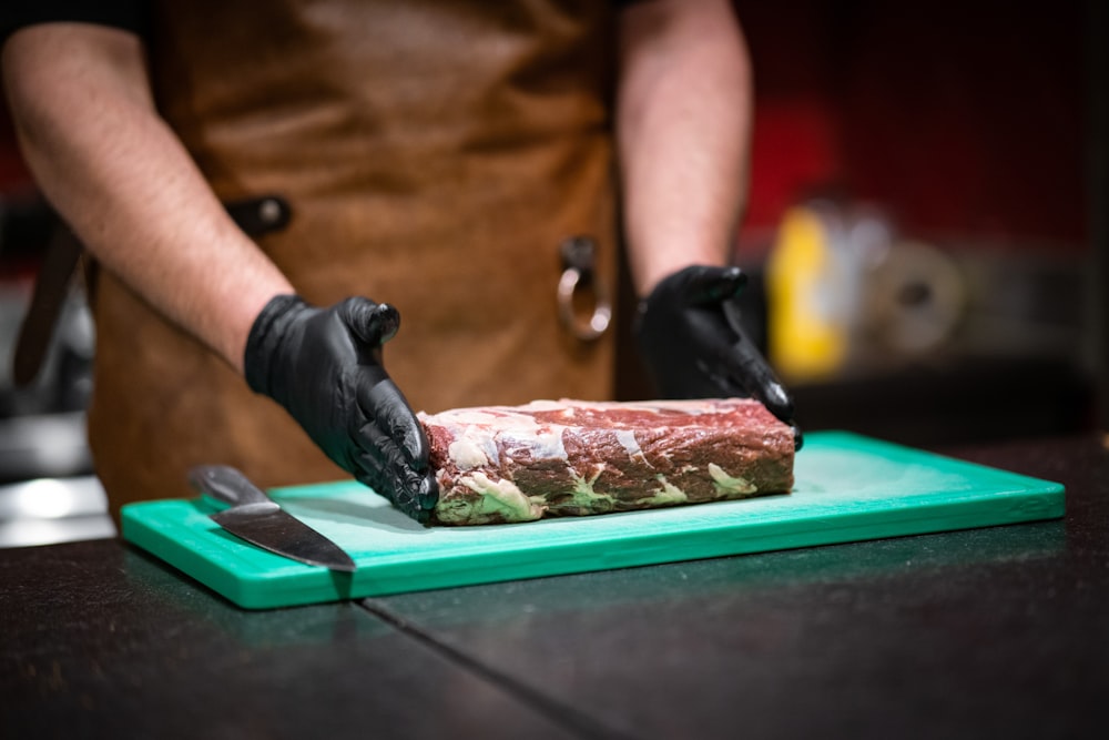 a person in black gloves cutting a piece of meat on a green cutting board