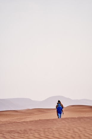 a person walking across a desert with mountains in the background