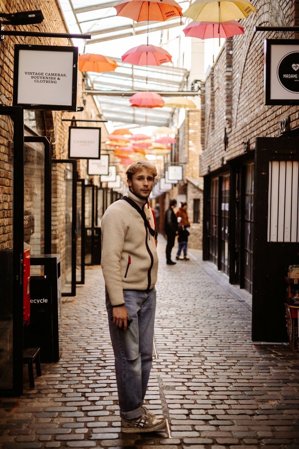 a man standing on a brick street under umbrellas