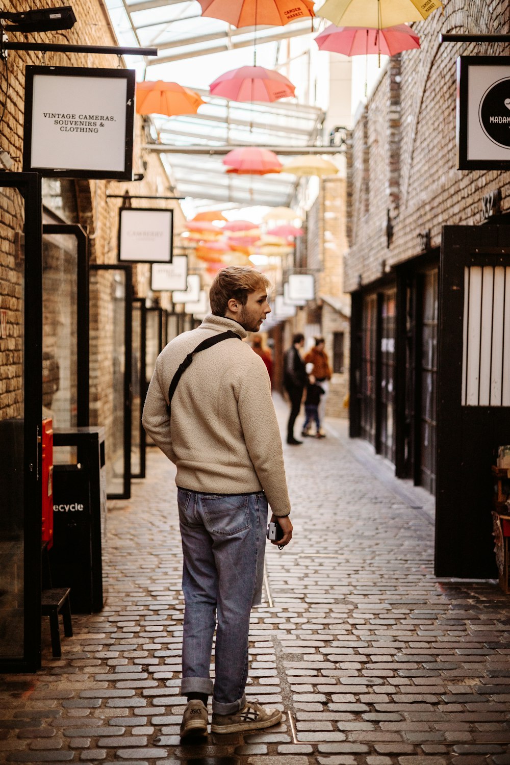 a man walking down a brick street under umbrellas