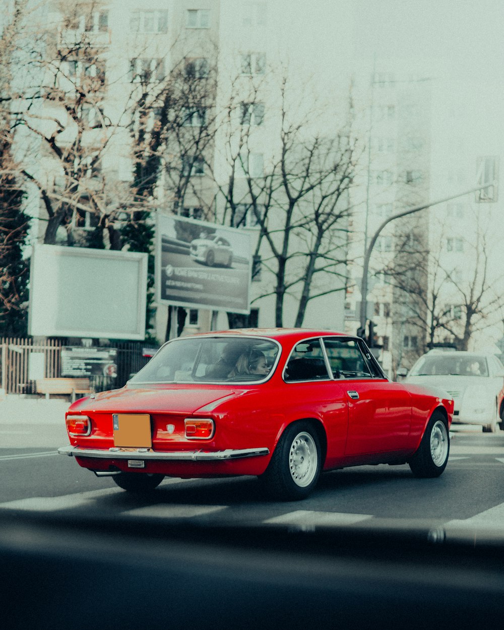 a red car driving down a street next to tall buildings