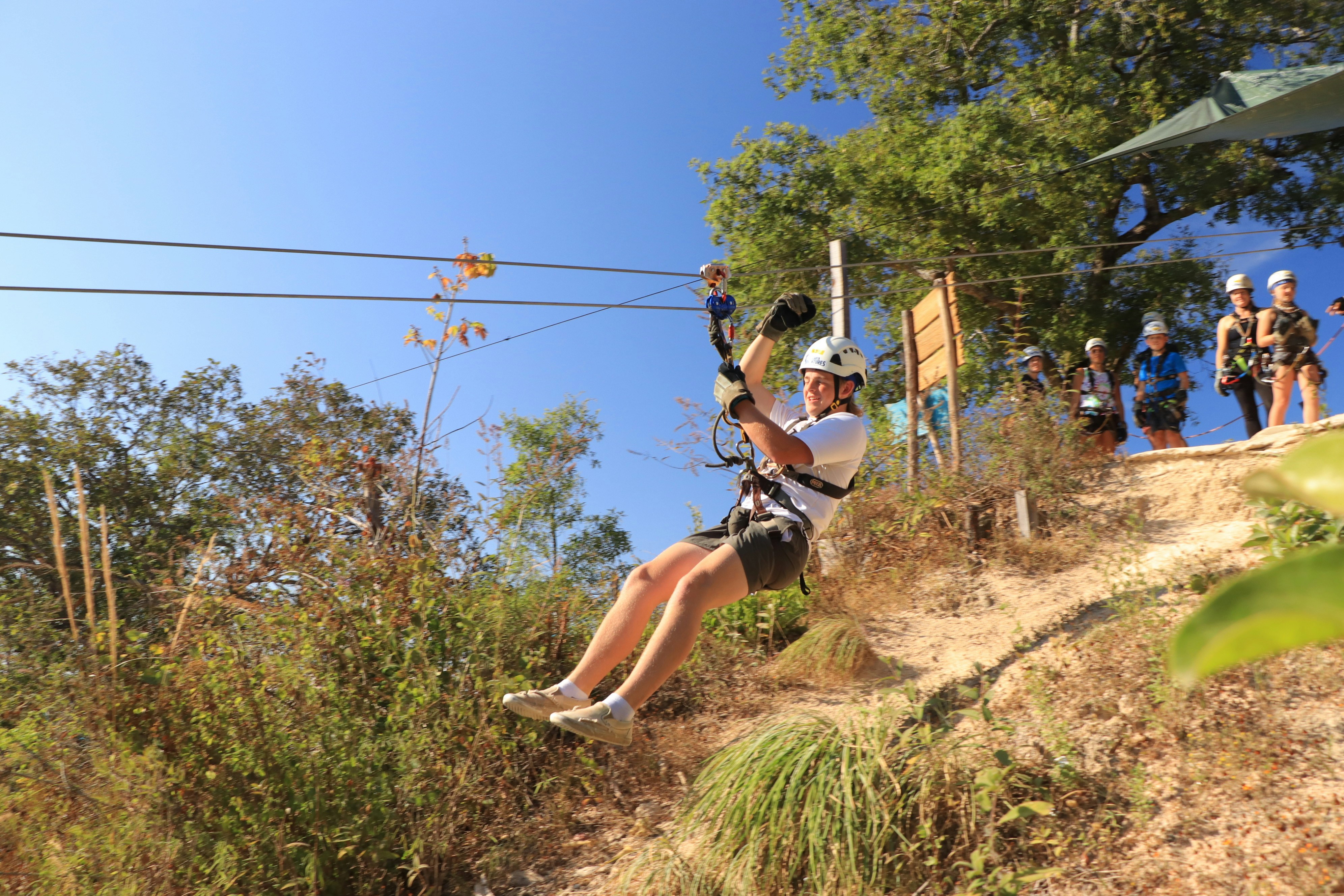 a man riding a zip line on top of a lush green hillside