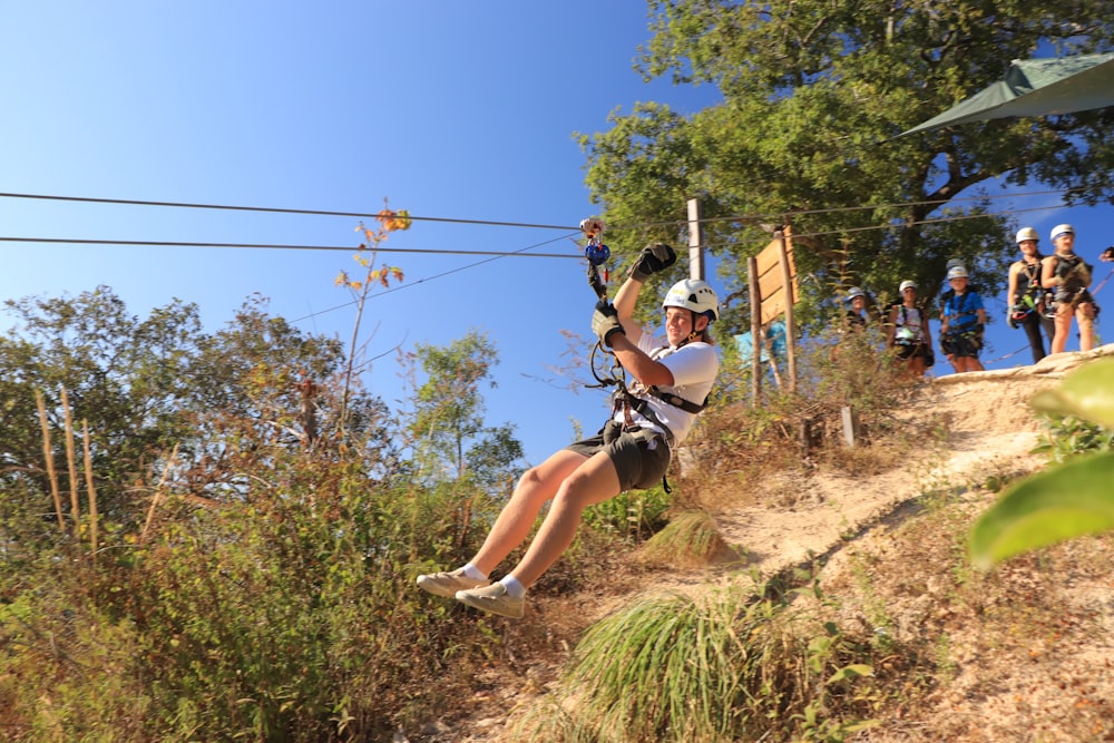 a man riding a zip line on top of a lush green hillside