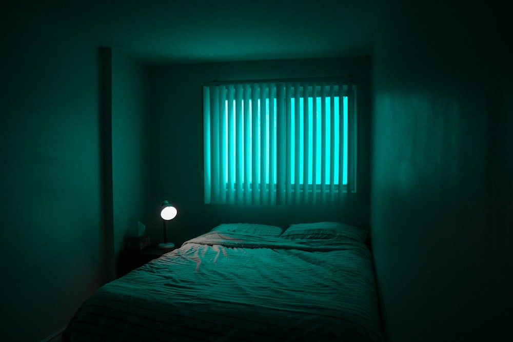 a bed in a dark room with a green light coming through the window