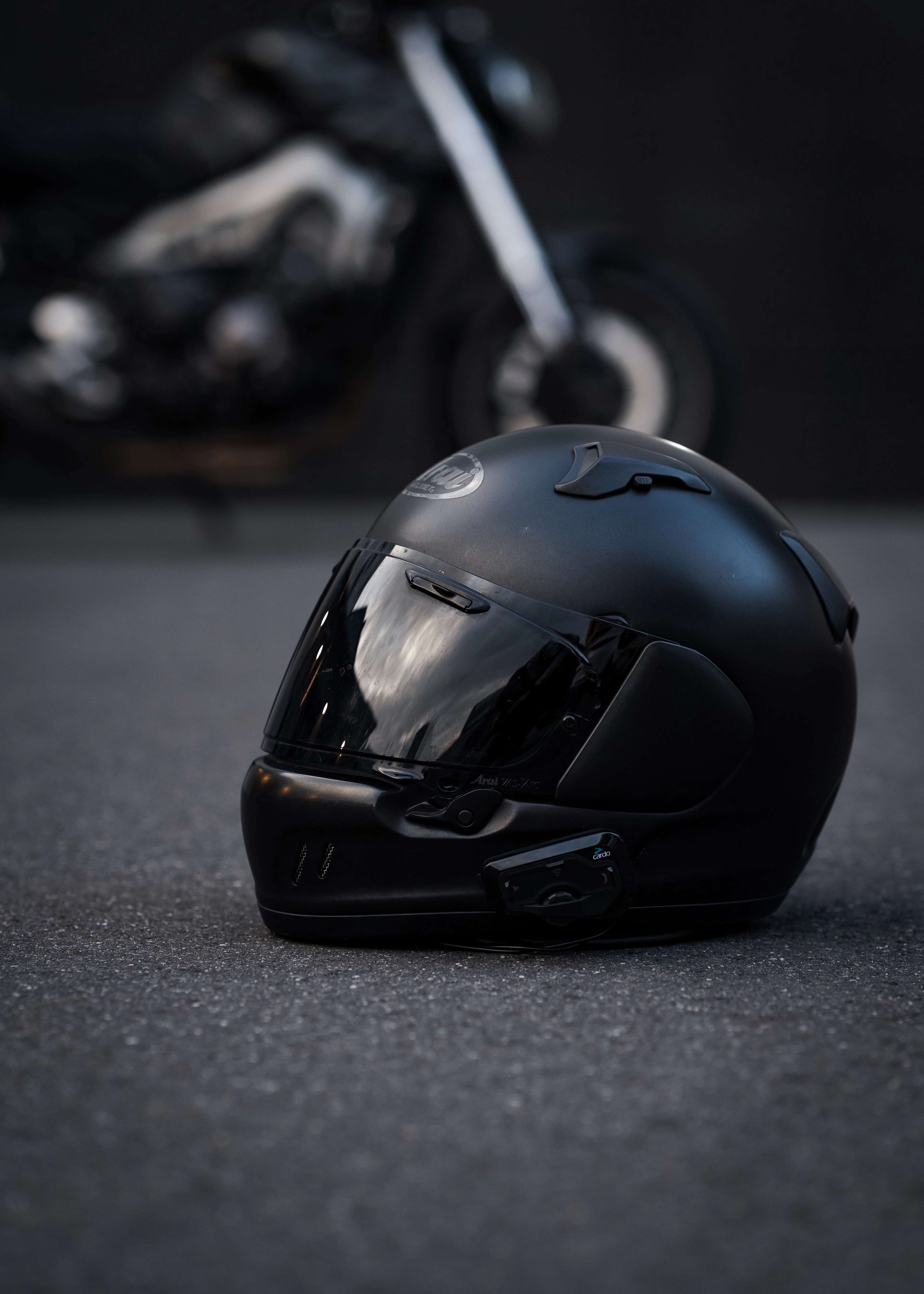Matte black full-face helmet with a dark visor, resting on asphalt
