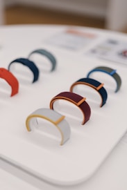 Several colorful wristbands are neatly displayed on a white stand. The bands come in a variety of colors, including red, blue, grey, and burgundy. The focus is on the design and color diversity of the bands, laid out in two rows.
