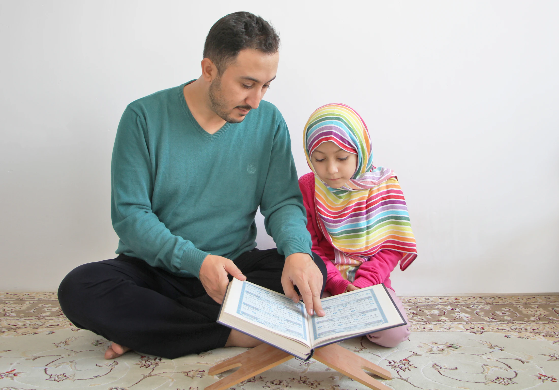 A parent reading the Quran together with their young daughter